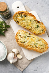 Two halves of garlic and butter bread - baguette on a marble board, sea salt, pepper, dill and garlic cloves on a grey concrete background, top view