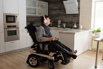 Man in wheelchair enjoying music in hedphones while sitting in large comfortable kitchen in the...