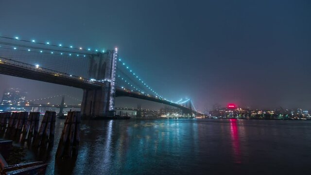 Timelapse of the illuminated suspension Manhattan bridge and Brooklyn bridge on the background. East River in New York City, USA. Night. Vessels sail along river, bright skyscrapers on another bank