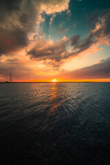 Vertical shot of the beautiful sunset above the sea. Oosterscheldekering, the Netherlands. - obrazy, fototapety, plakaty