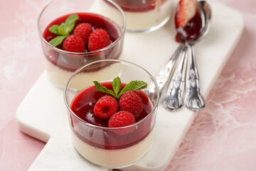 Italian dairy dessert panna cotta with raspberry jam, fresh raspberries and mint on marble board on pink surface