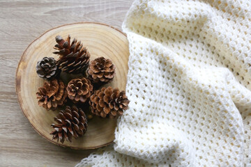 Wooden tray with pine cones and soft knitted blanket. Hygge at home. Flat lay.