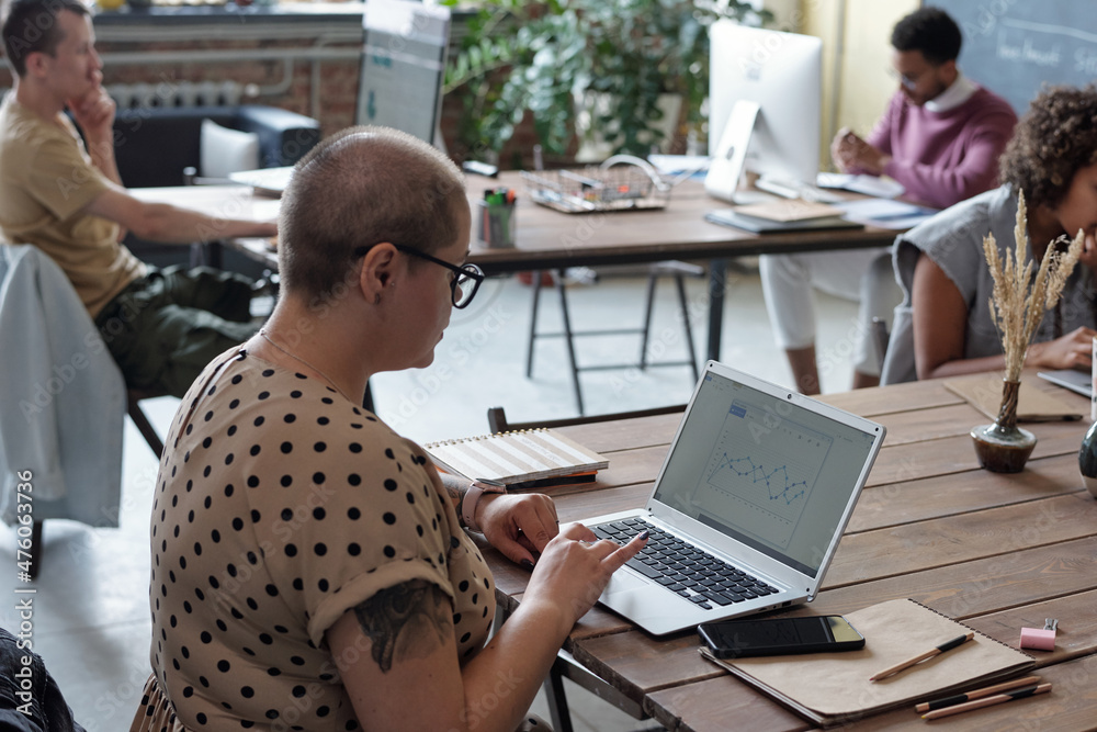 Poster busy office worker sitting by table in front of laptop and looking at financial graph on screen amon