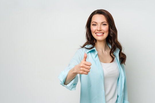 Attractive young woman , brunette, with a beaming smile, giving a thumb up gesture of approval and success.