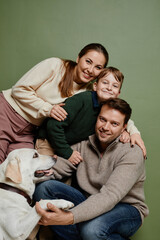 Vertical portrait of loving family with son and dog smiling at camera against green background