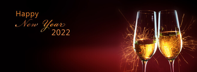 Happy New Year 2022 text, party time with two champagne glasses and fireworks of sparklers against...