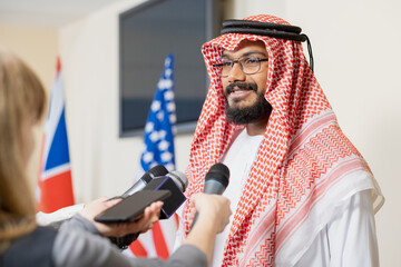 Young Arabian businessman in national clothes giving interview to journalists after political event in conference hall