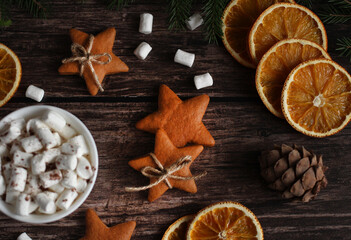 mug with marshmallows, ginger cookies with stars, orange slices, cones on a wooden background
