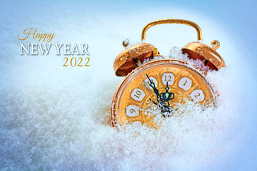 copper colored vintage alarm clock in the snow pointing five minutes before twelve, text Happy New Year 2022, seasonal greeting card with copy space