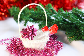 Test tubes with a vaccine against the COVID-19 coronavirus lie as a gift in a basket against the background of New Year decorations. Close-up. The concept of holidays