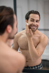 Fototapeta na wymiar Half-naked man standing near at the mirror and applying shaving foam on his face