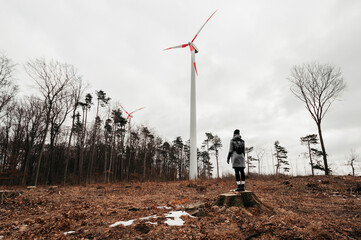 Woman standing and looking on  wind turbine station in destroyed and deforested forest on tree...
