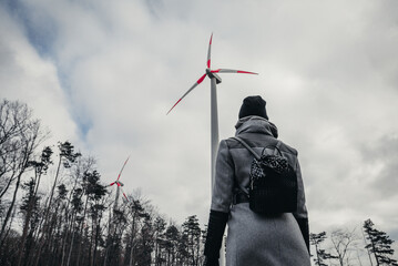 Woman standing and looking on  wind turbine station near forest  in bad weather conditions -...