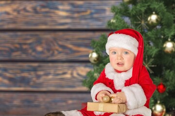 Cute child with Christmas tree. Happy baby sitting near a fir tree and holding a Christmas ornament