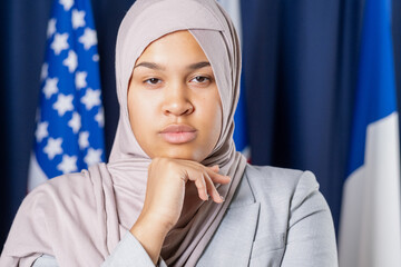 Young serious female delegate or political leader in hijab looking at camera while keeping hand under chin - Powered by Adobe
