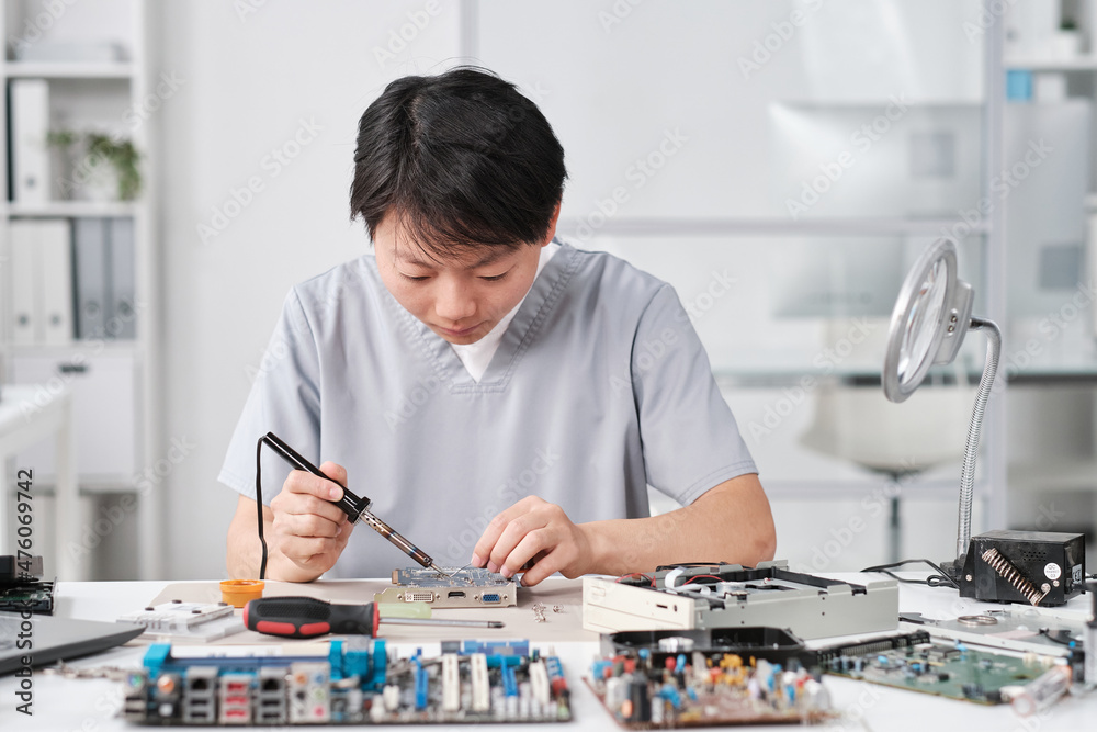 Poster young chinese female technician in uniform repairing circuit board with microprocessor while sitting