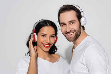 cheerful young couple in headphones looking at camera while listening music on grey. - Powered by Adobe