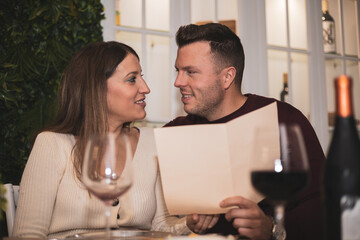 Beautiful young adult couple looking at menu to order food in restaurant while passionately looking at each other.