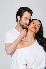 man with closed eyes touching neck of passionate woman with bare shoulder isolated on grey.