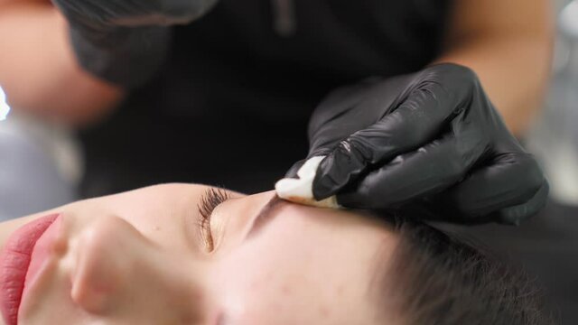 Master makes permanent eyebrow makeup procedure using special needle tattoo machine to woman in beauty salon. Microblading brows tattooing. Dark pigment is injected under skin. Cosmetology procedure