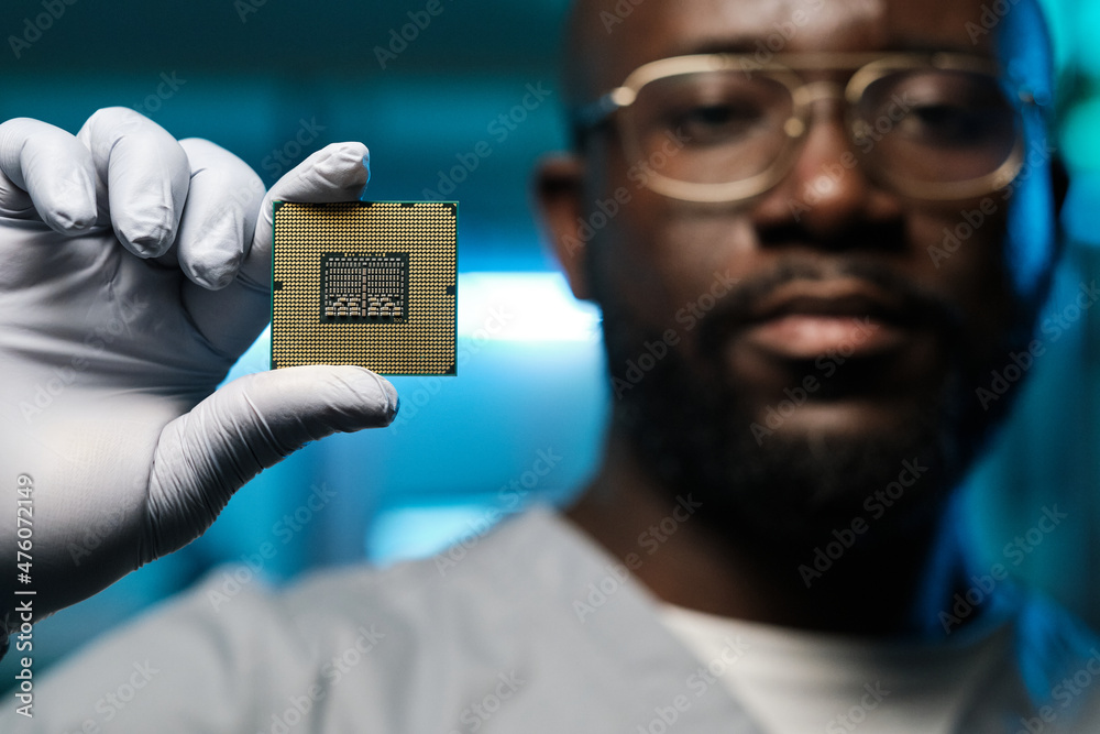 Poster gloved hand of contemporary technician of african ethnicity showing microchip while holding it in fr