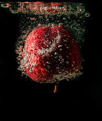 Obraz na płótnie Canvas Red apple falling into water against a black background.