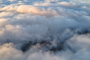 Aerial view from high altitude of distant city covered with puffy cumulus clouds flying by before...
