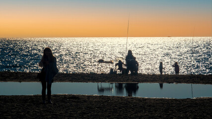Siluetas de gente en la orilla de la playa pescando