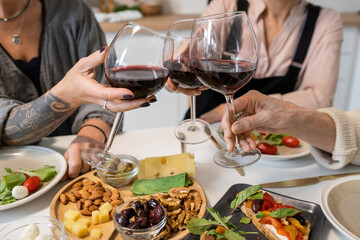 Close-up of women toasting with glasses of red wine while sitting at dining table with appetizers