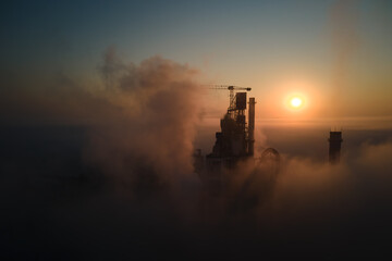 Aerial view of cement factory with high concrete plant structure and tower crane at industrial production site on foggy morning. Manufacture and global industry concept - obrazy, fototapety, plakaty