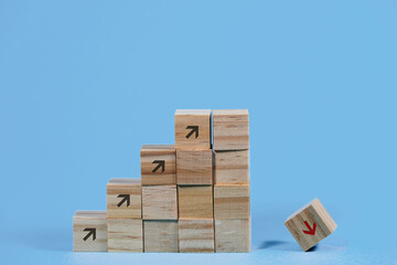 Wooden cubes build as stair steps with arrows pointing upwards, but the last cube is falling down, concept for the risk of failure due to overly rapid business growth, blue background with copy space
