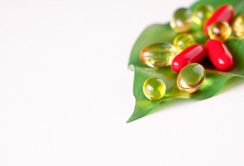 Concept alternative medicine. Red and yellow capsules of vitamins lying on green leaf on white background macro. Copy space
