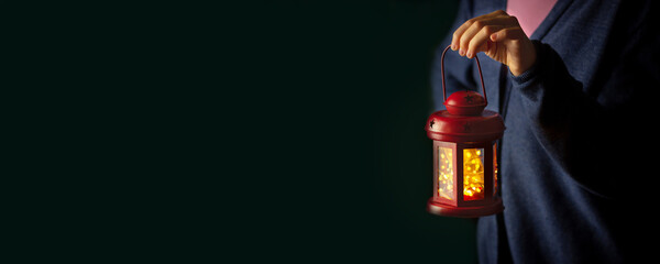 red christmas lantern held in hand in the dark with copy space. festive banner with place for text. lack of electricity © x.marynka