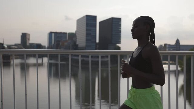 Active woman in sportswear jogging on bridge over river