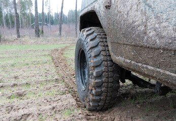 Fototapeta premium Photo of an off-road black car on muddy gravel road. Rally racing SUV in the forest with trees. Automobile wheel with tire