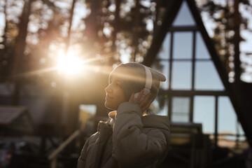 A teenage girl on the background of sunset and mirrored windows of the house wearing headphones. The concept of life after quarantine. High-quality photography