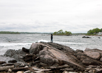 Lone adventurer standing atop of a boulder on a rocky coast. Portland, Maine.