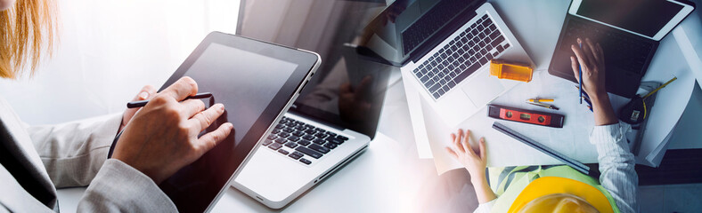 Two colleagues discussing data working and tablet; laptop with on on architectural project at construction site at desk in office