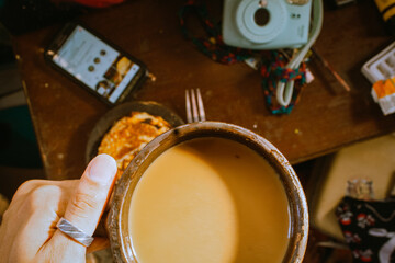 Closeup of a person holding a cup of hot chai tea above a messy table with pancakes on it