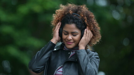 Happy Brazilian woman listening to music wearing headphone in street