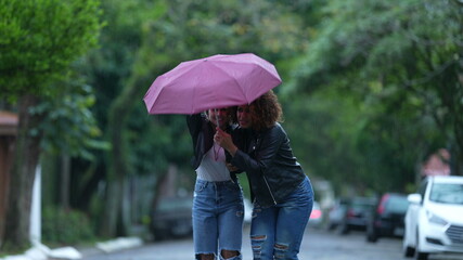 Female friends opening umbrella walking in city during rainy day