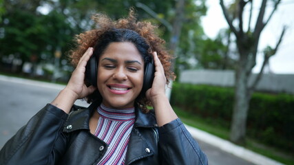 Fototapeta premium Carefree black woman dancing to music outside in street wearing headphones