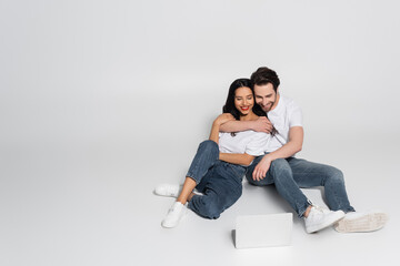 happy couple in casual clothes watching movie on laptop on grey.