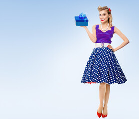 Full body portrait of smiling woman dressed in pin-up style dress with polka dot, over light blue background. Blonde pinup girl posing in retro fashion and vintage concept studio shot.