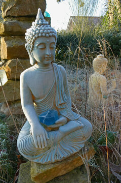 A blue Buddha statue with a piece of blue glass on his lap covered with hoarfrost. In the background a white Buddha