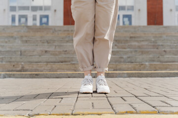 female legs in white sneakers stand on the sidewalk near the stairs