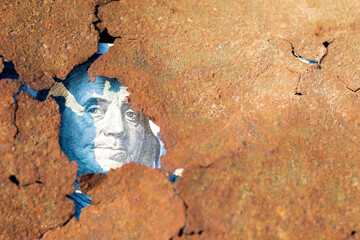 a portrait of the president from a hundred dollar bill peeps through a broken piece of rusty iron sheet