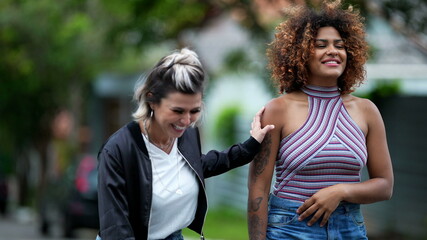 Obraz premium Candid two diverse women walking together outside in street laughing and smiling