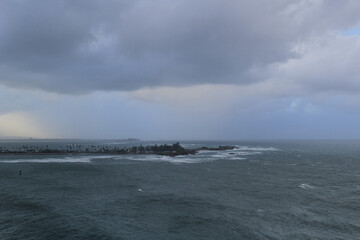 Stormy ocean with cloudy sky, with island in a background, view from Castillo San Felipe del Morro, Puerto Rico - obrazy, fototapety, plakaty