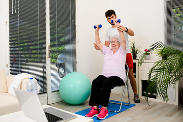 senior elderly woman with a personal trainer private fitness coach at home handsome young man